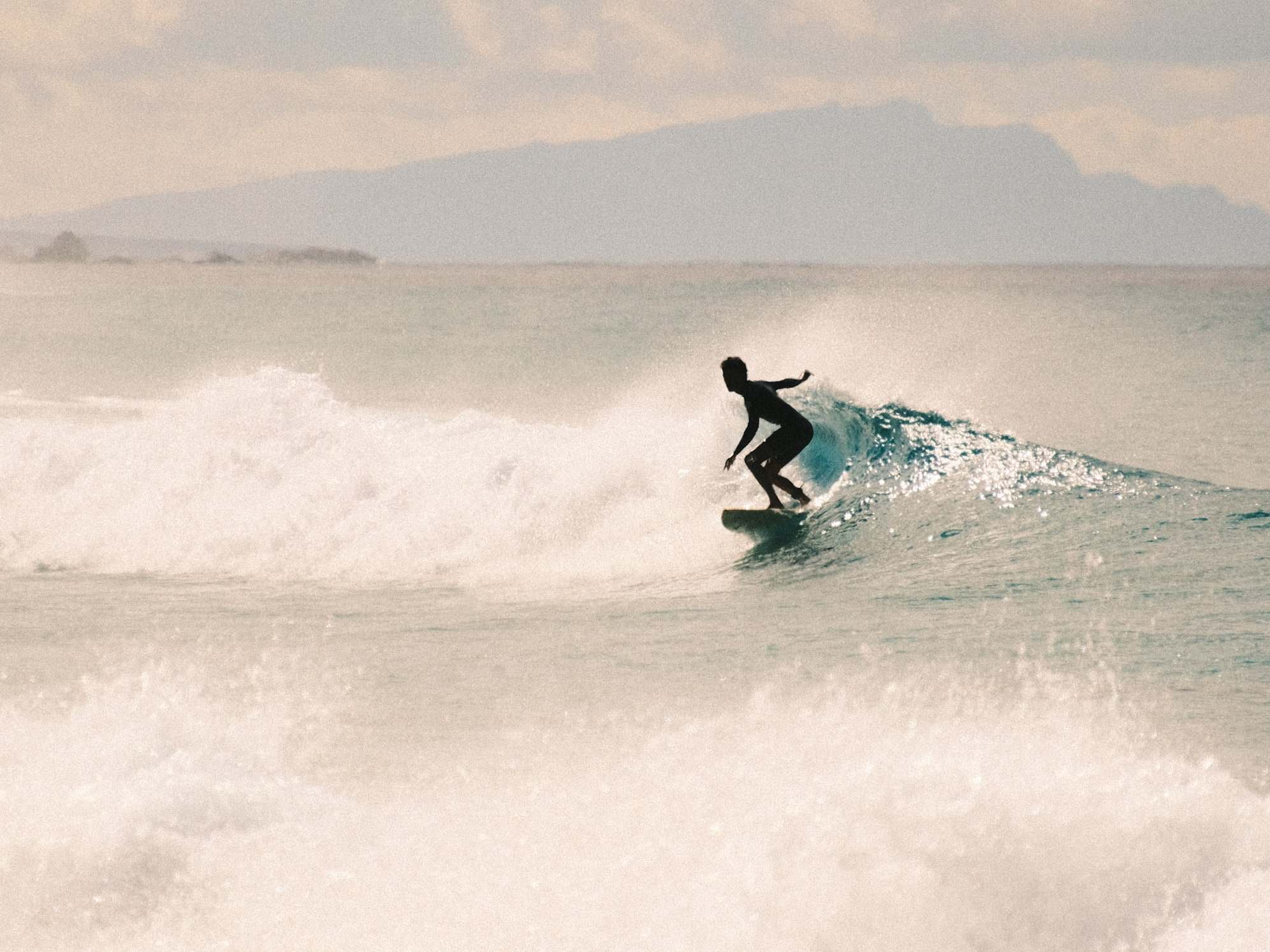 Backlit surfer carving through spray with an island silhouette behind