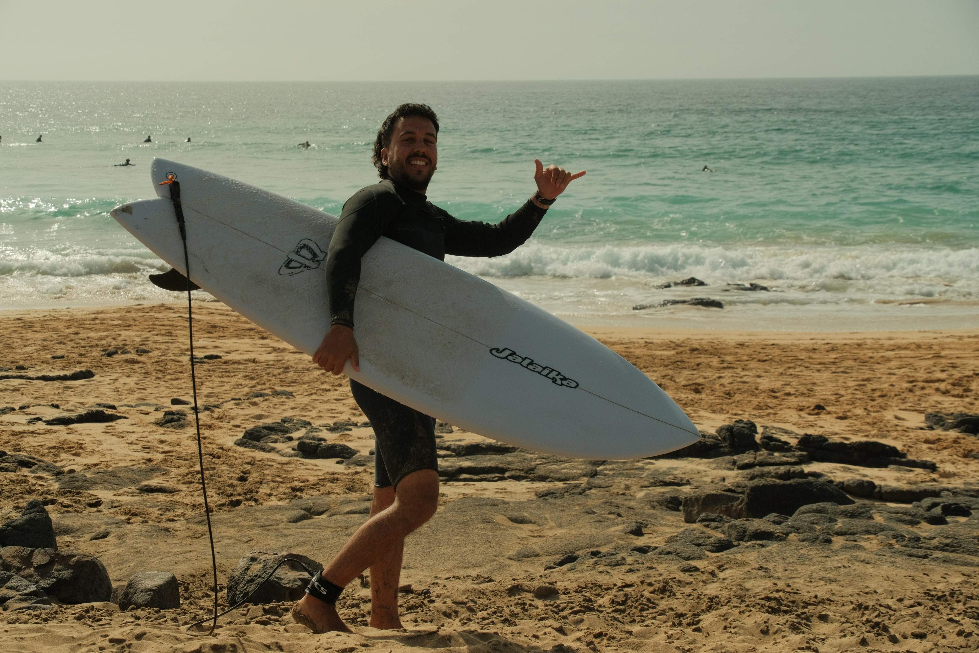 Erik, surf photographer in Fuerteventura, holding his surfboard and throwing a shaka