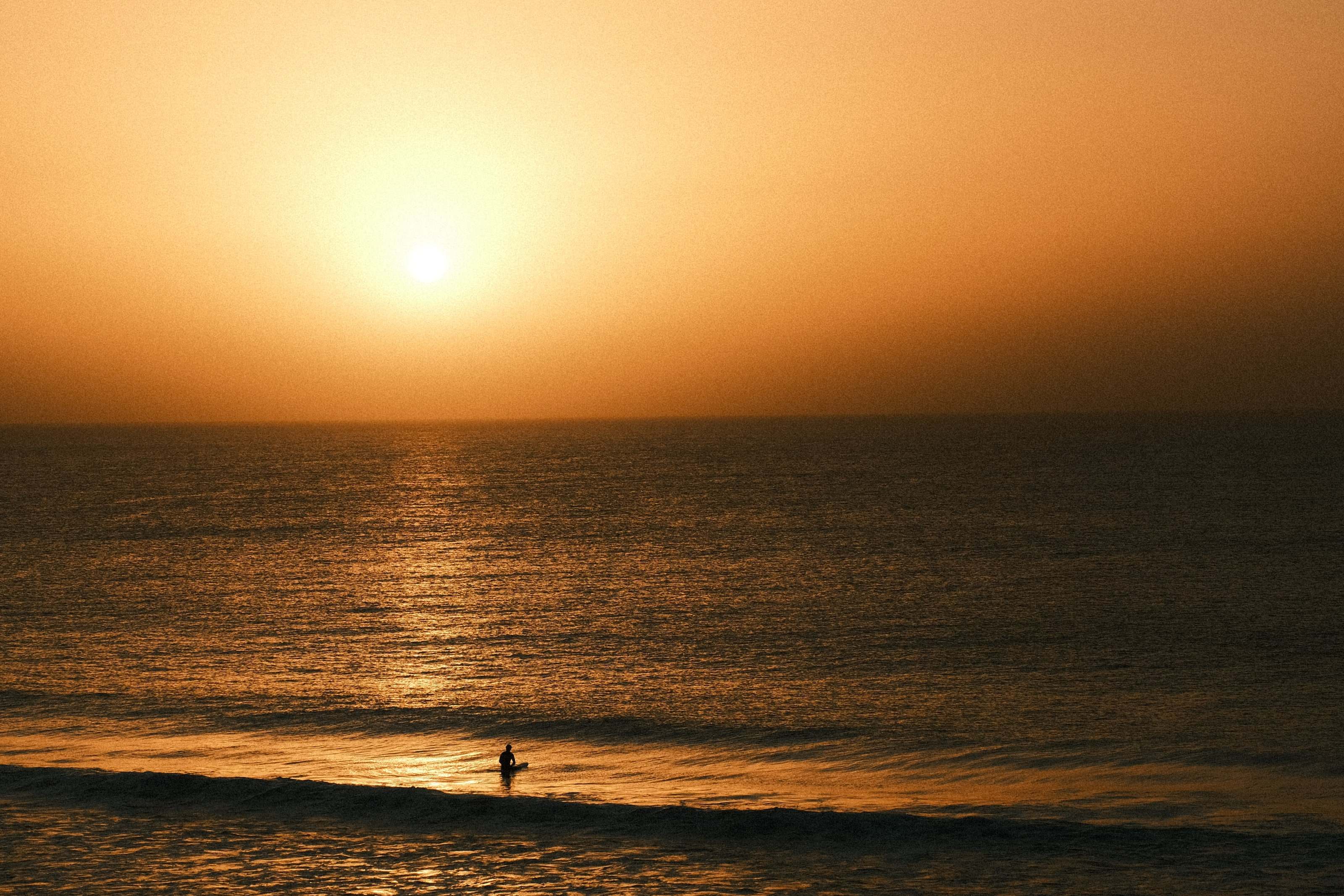 Lone surfer sitting on the board as the sun sets over the Atlantic