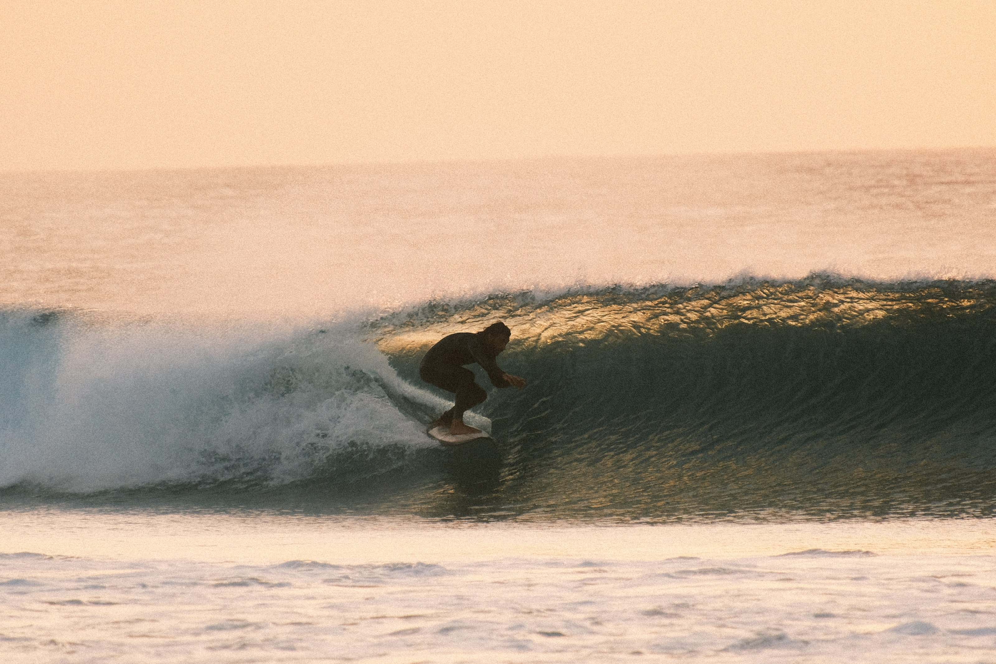 Backlit surfer pulling into a golden barrel at sunset in Fuerteventura