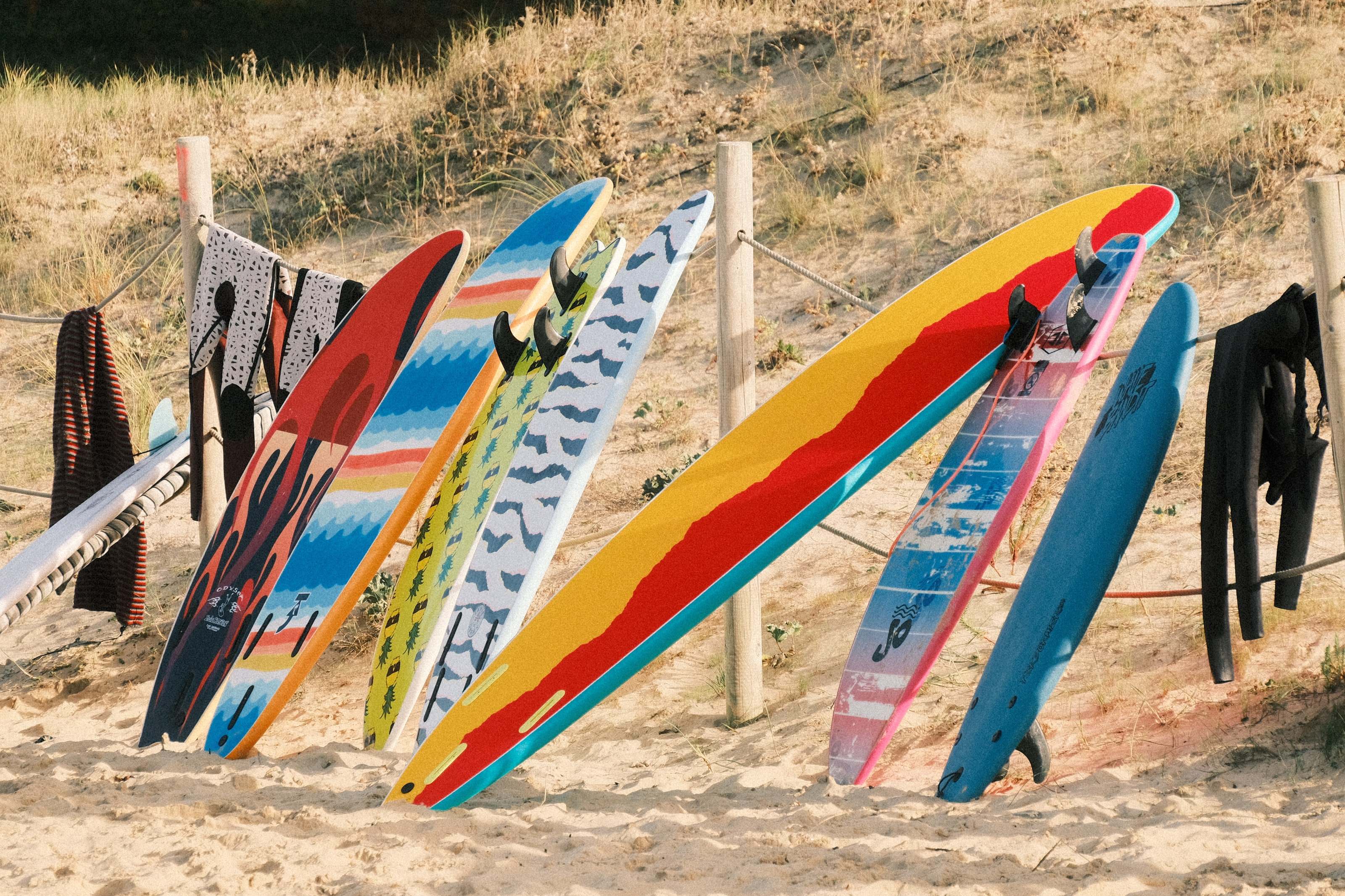 Colourful surfboards and wetsuits leaning on a fence in the dunes