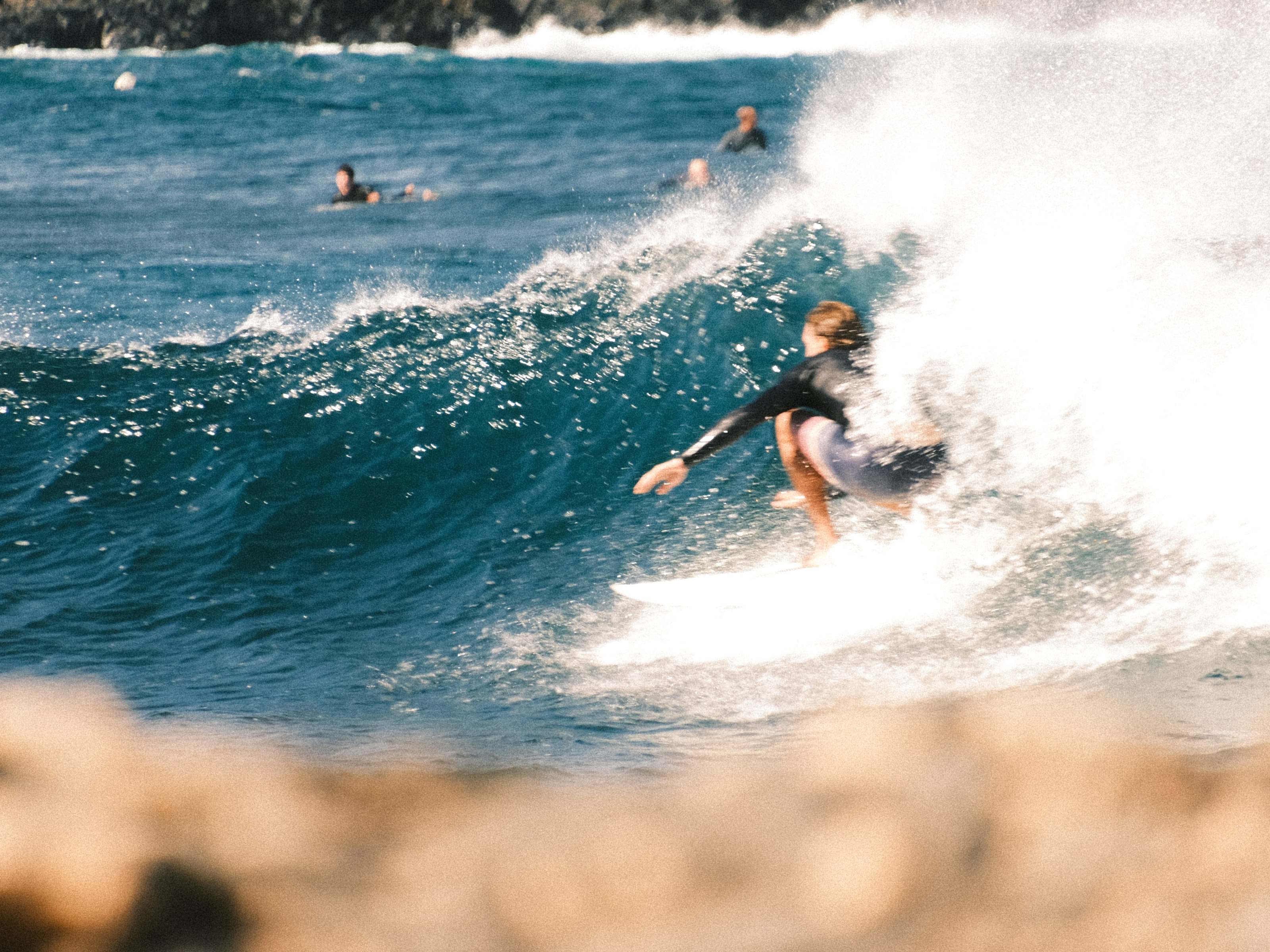 Surfer turning off the top on a reef break, volcanic rock blurred in the foreground