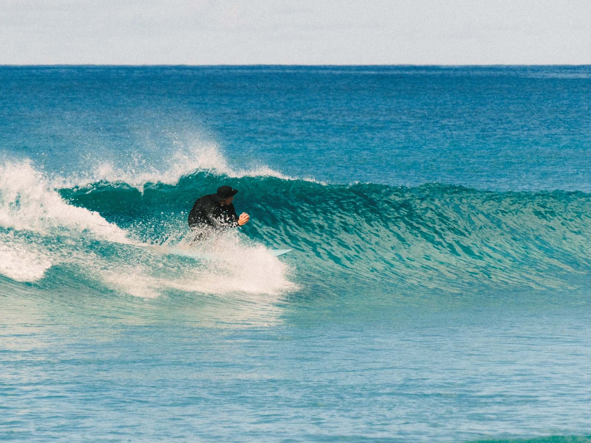 Surfer in a cap racing down a turquoise wave wall in Fuerteventura