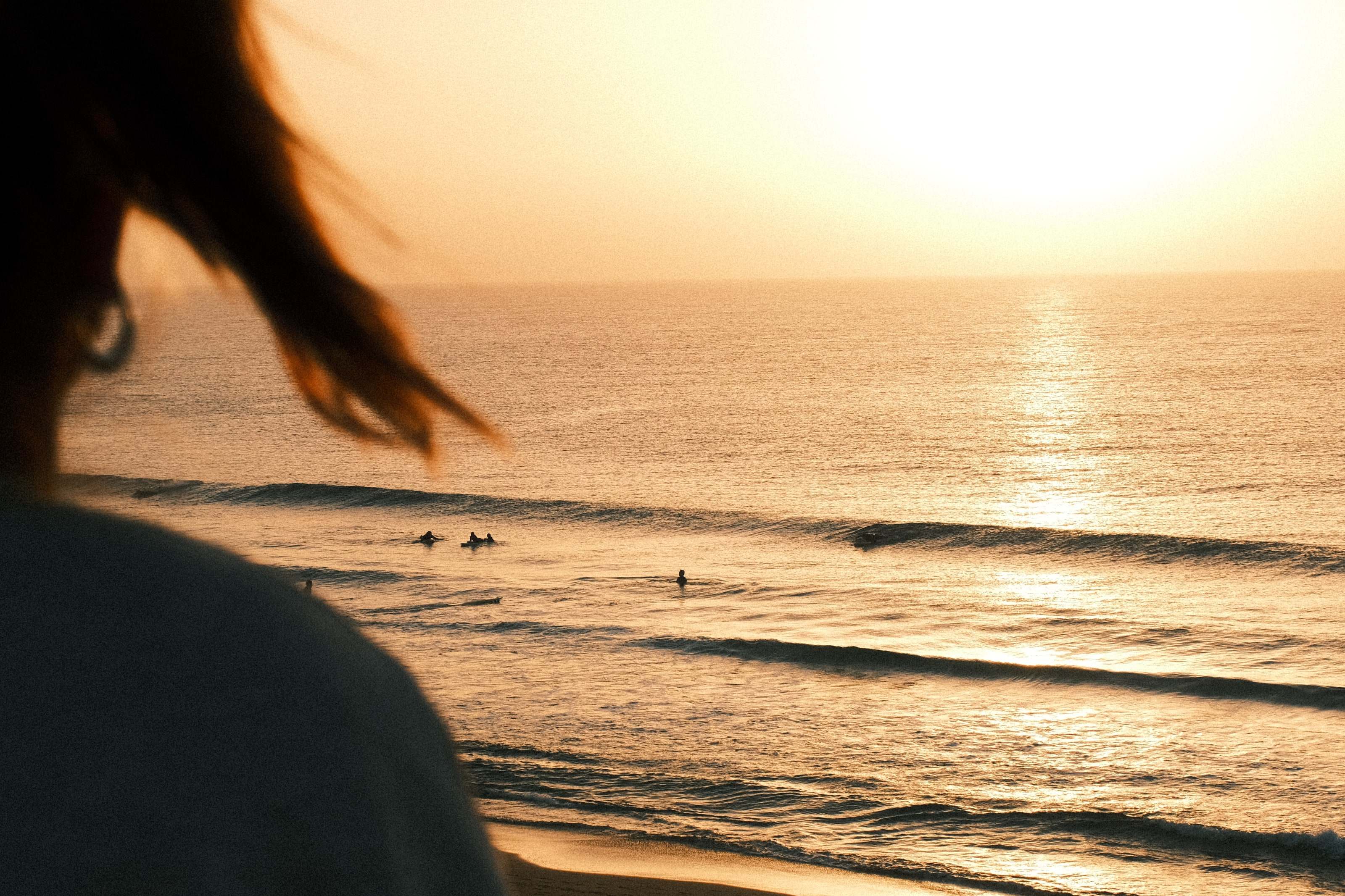 Woman with windblown hair watching surfers in the sunset line-up
